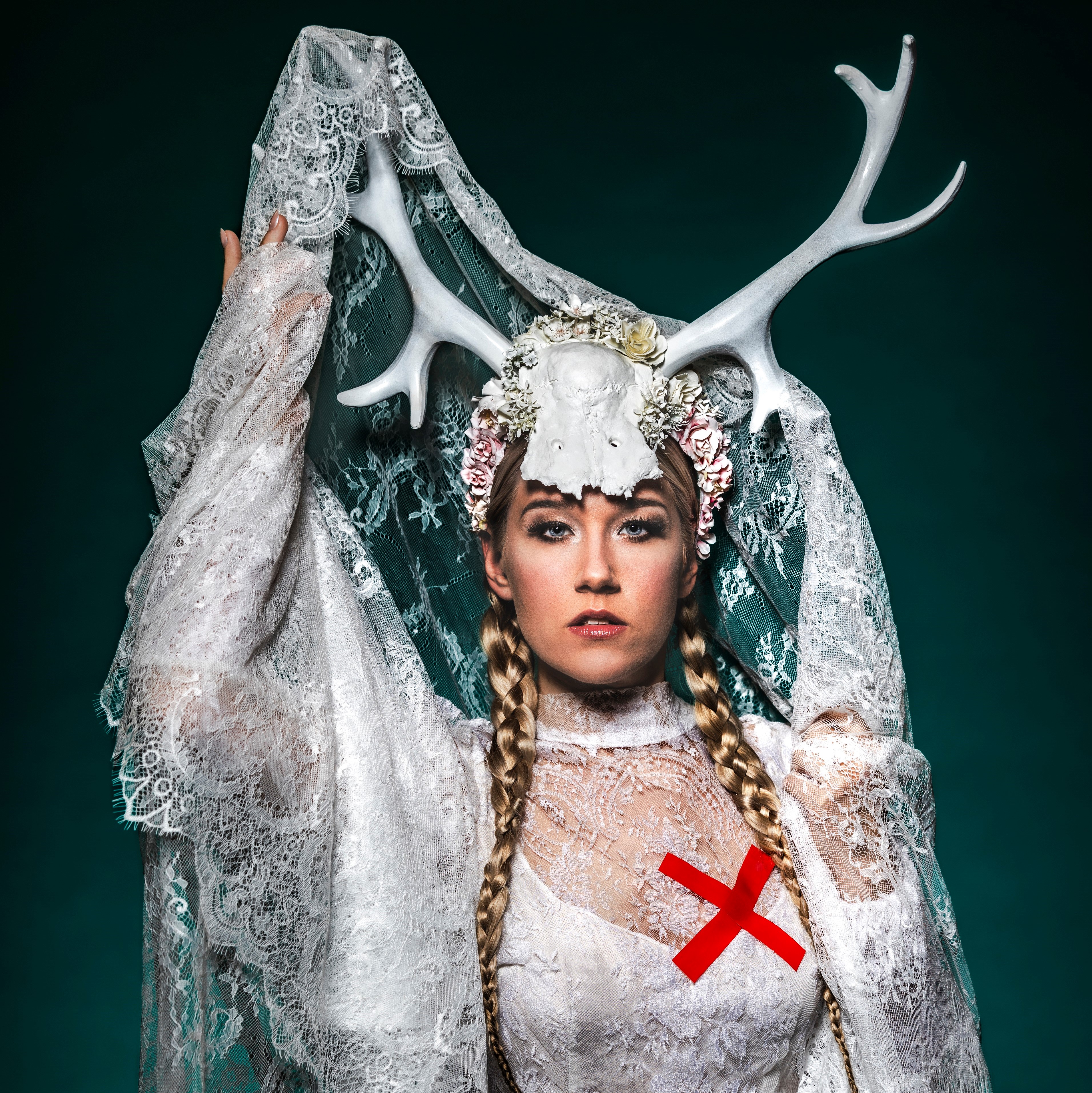 Plakatmotiv Der Freischütz, Foto: Jochen Quast Eine Frau (Lavinia Husmann) in weißem Kleid und Schleier mit Geweih-Kopfschmuck vor dunklem Hintergrund. Sie hat rotes X auf der Brust Foto: Jochen Quast